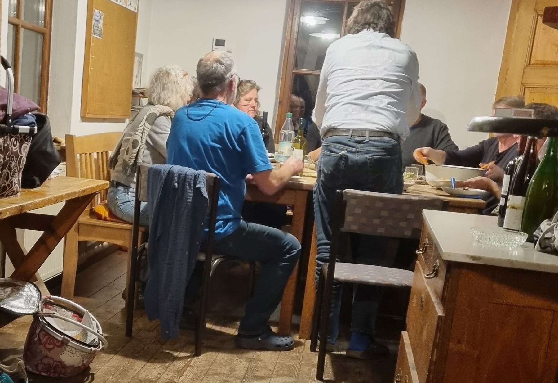 Die Teller füllen sich weiter, fast leere Korktafel und Heizungsthermostat im Hintergrund, das besonders Diskussionsstoff lieferte. Denn mit einem Außentemperaturfühler handelt es sich um ein modernes elektronisches Gerät, das die Außentemperatur misst. Die Daten sendet der Fühler an die Heizungssteuerung, die dann die Vorlauftemperatur der Heizungsanlage an der gemessenen Außentemperatur ausrichtet. Der Außenfühler besitzt für die Messung im Inneren ein temperaturabhängiges Element, das auf steigende oder fallende Temperaturen reagiert. Fällt die Außentemperatur, erhöht die Heizungsanlage die Vorlauftemperatur. Wie stark diese erhöht wird, hängt von der individuellen Heizkurve in Ohlweiler ab. Die Heizkurve wurde deshalb im Vorfeld berechnet, unter Berücksichtigung der Wärmedämmung. Steigt die Außentemperatur in Ohlweiler, regelt die Heizungssteuerung die Vorlauftemperatur entsprechend herunter.